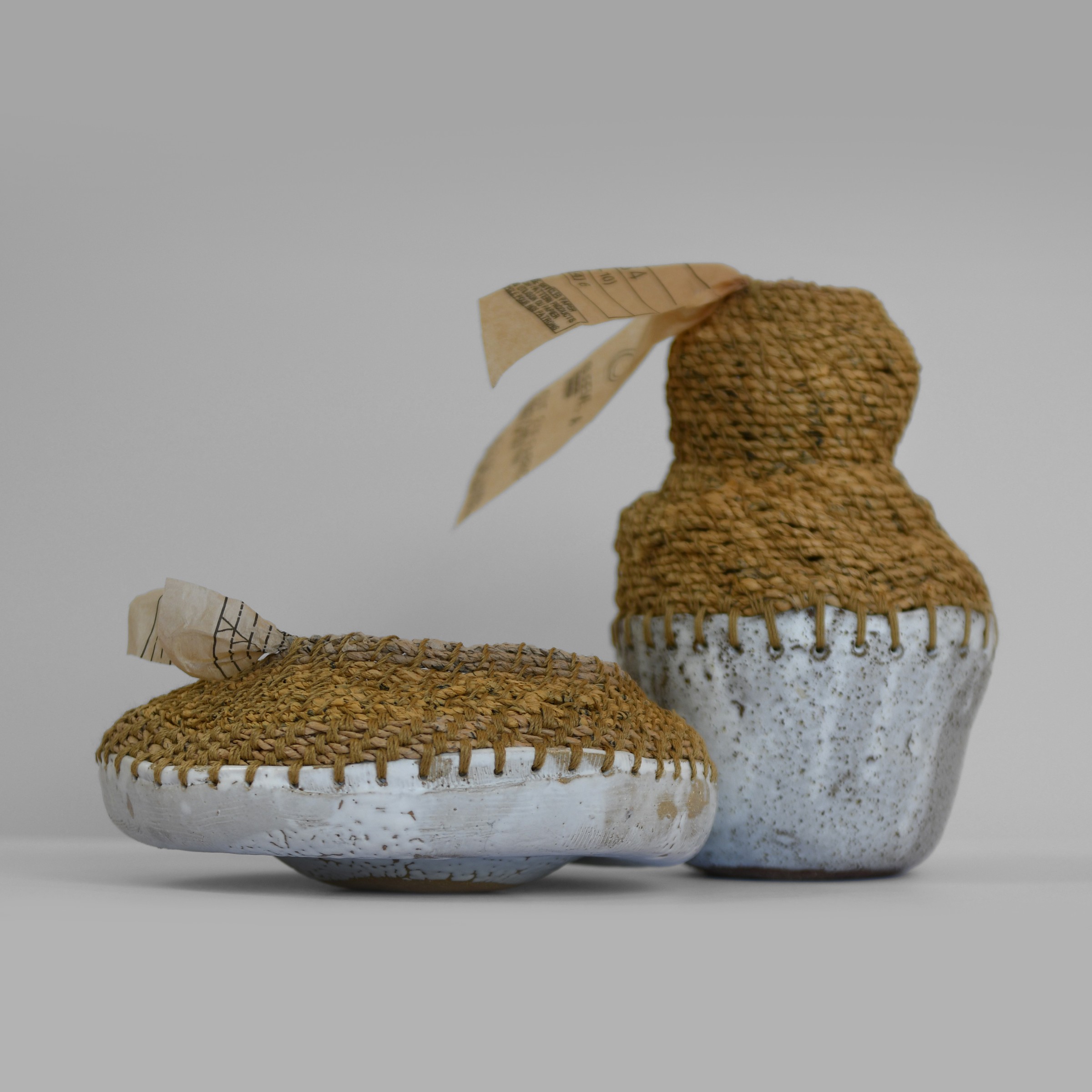 Two pale ceramic forms continued with woven sewing-pattern tissue and loose paper ends.