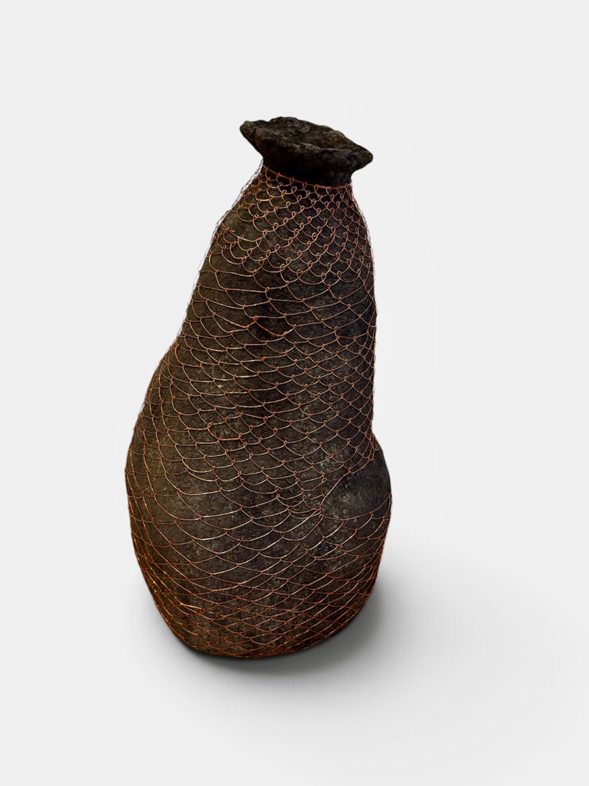 A dark, asymmetrical paper vessel enclosed in fine copper-coloured wire weaving.