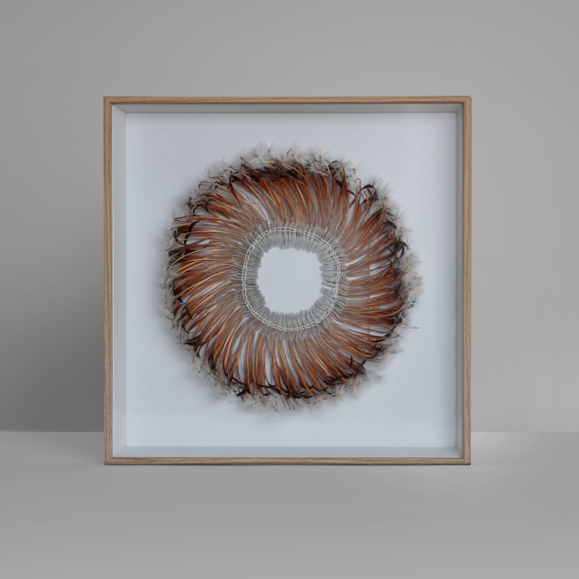 A framed circular bloom woven from dried native flowers, with an open centre and radiating brown strands.
